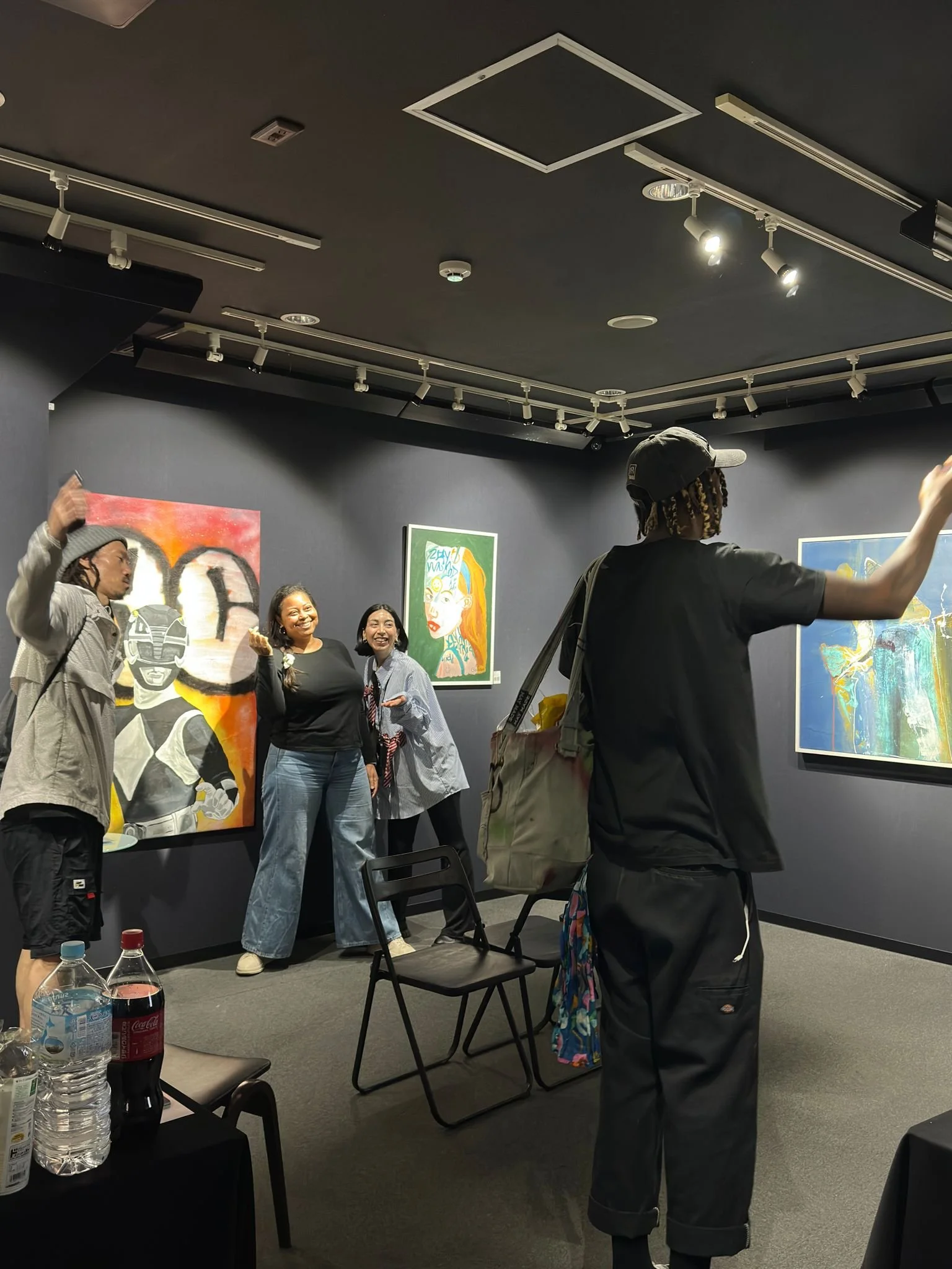 People standing and smiling in an art gallery with colorful artwork on dark walls and ceiling track lighting.