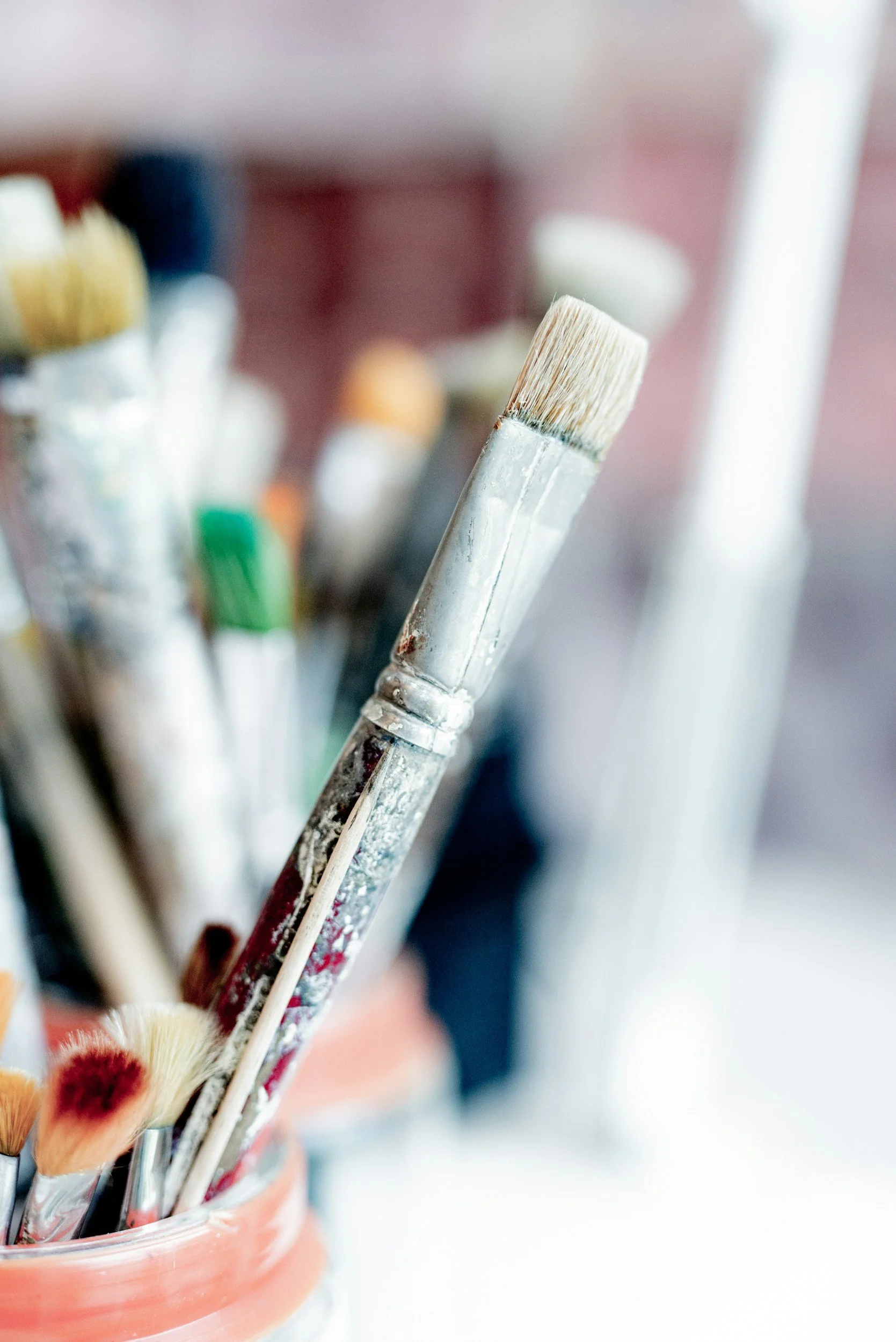 Close-up of paint brushes in a jar, with focus on a flat brush with white bristles.
