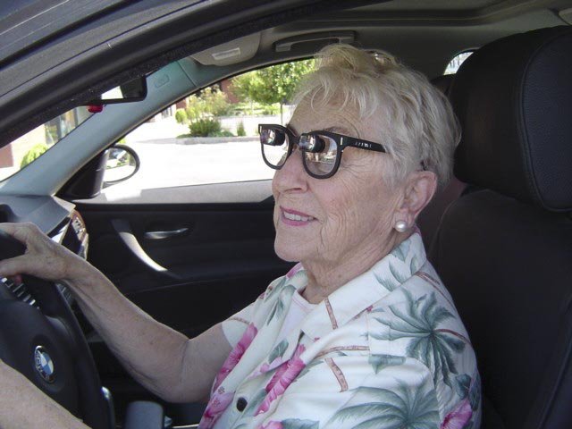 An older woman wearing special low vision glasses drives her car.