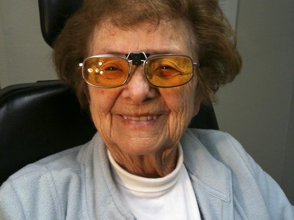 A woman wearing special low vision glasses smiles broadly at the camera.