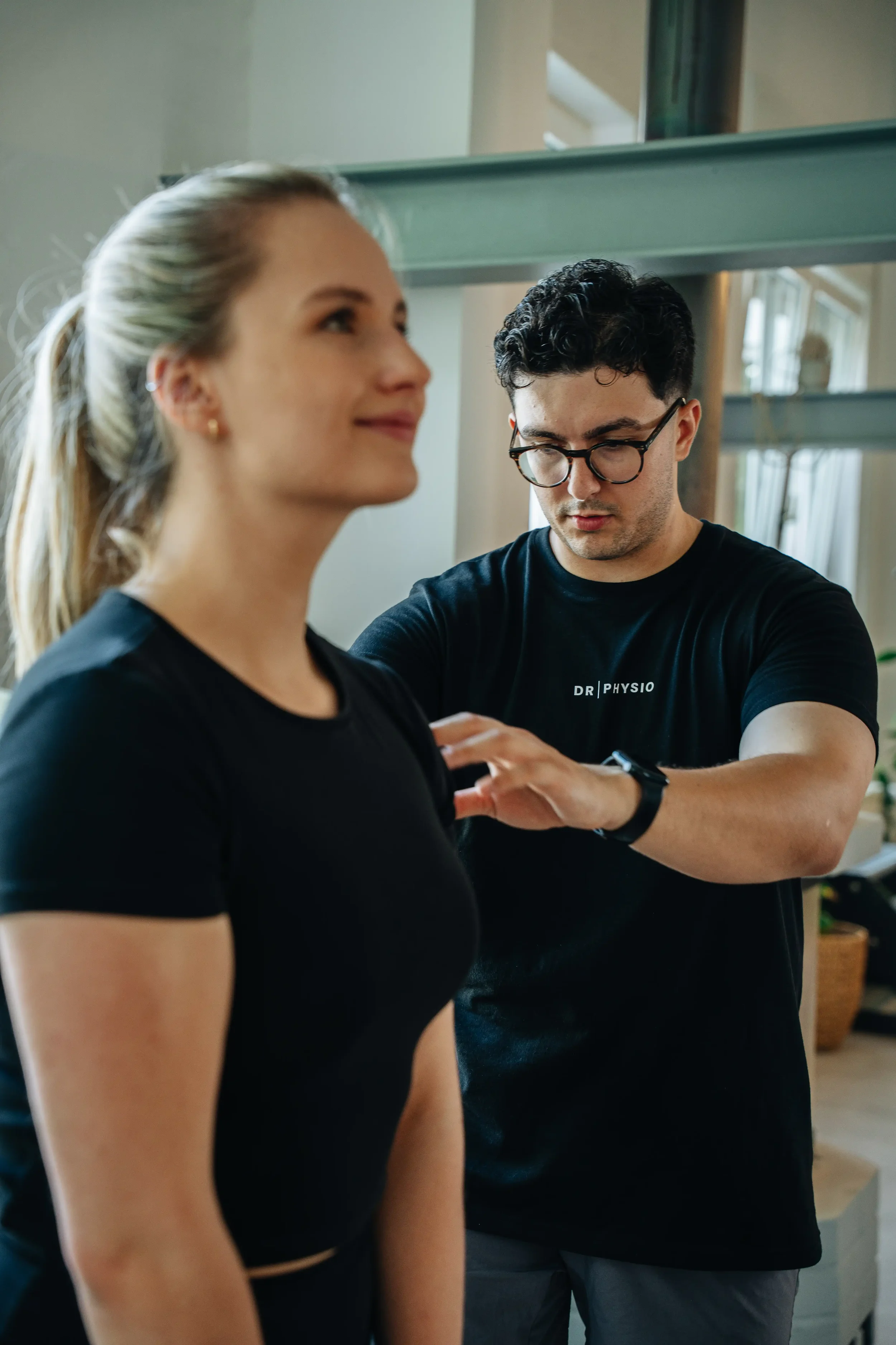 Mann misst die Schulter eines lächelnden Frauen während einer physiotherapeutischen Behandlung in einer Praxis