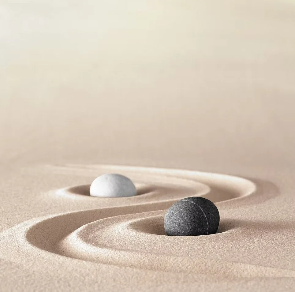 Two smooth stones resting in carefully raked, swirling sand patterns.