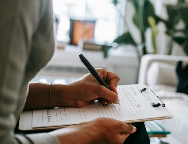 Person taking notes on a clipboard with a pen in a well-lit, modern office or living space.