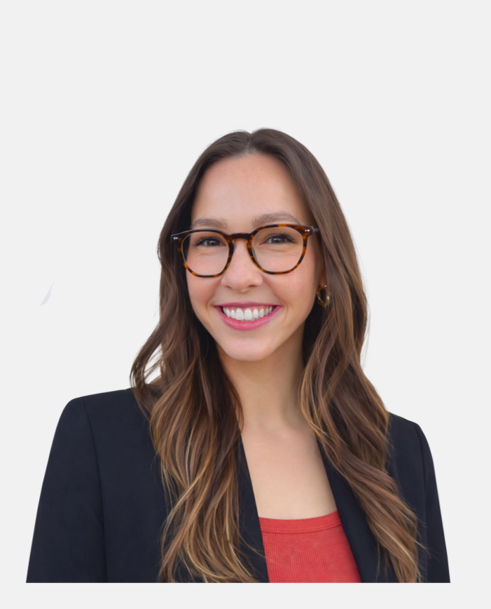 A smiling woman with long wavy brown hair, wearing glasses, a black blazer, and a red shirt, standing against a plain white background.