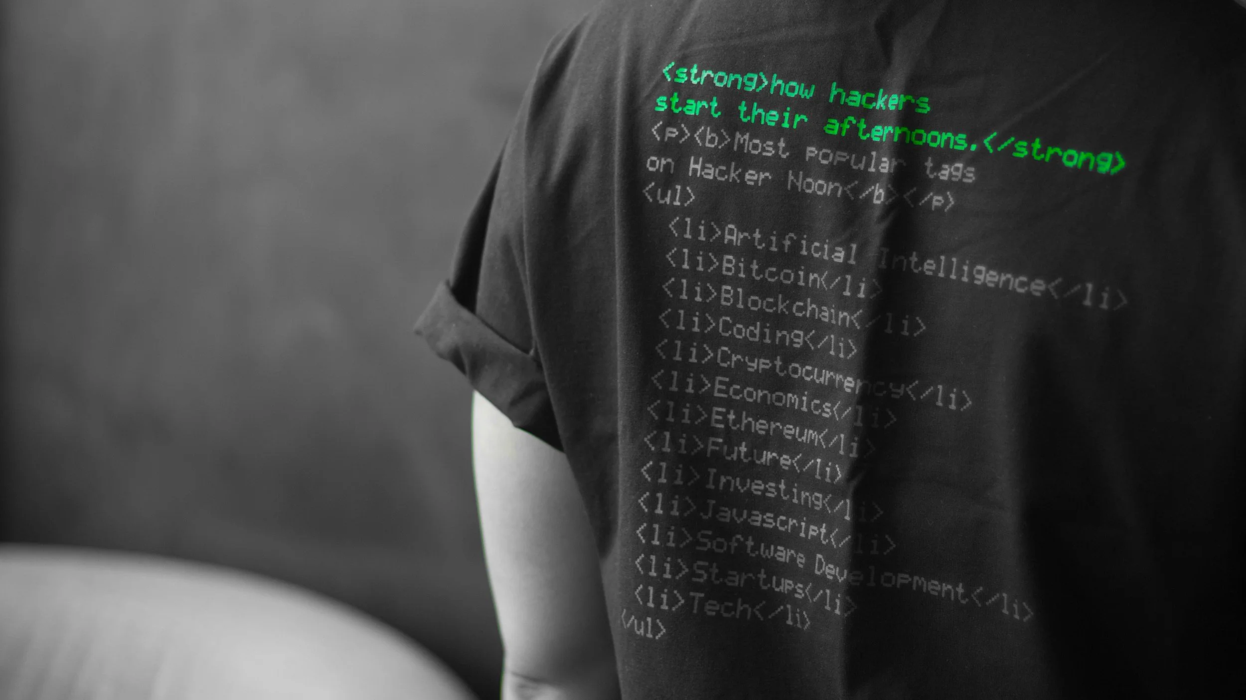 Person wearing a black T-shirt with green and gray computer code text printed on it, standing against a plain background.