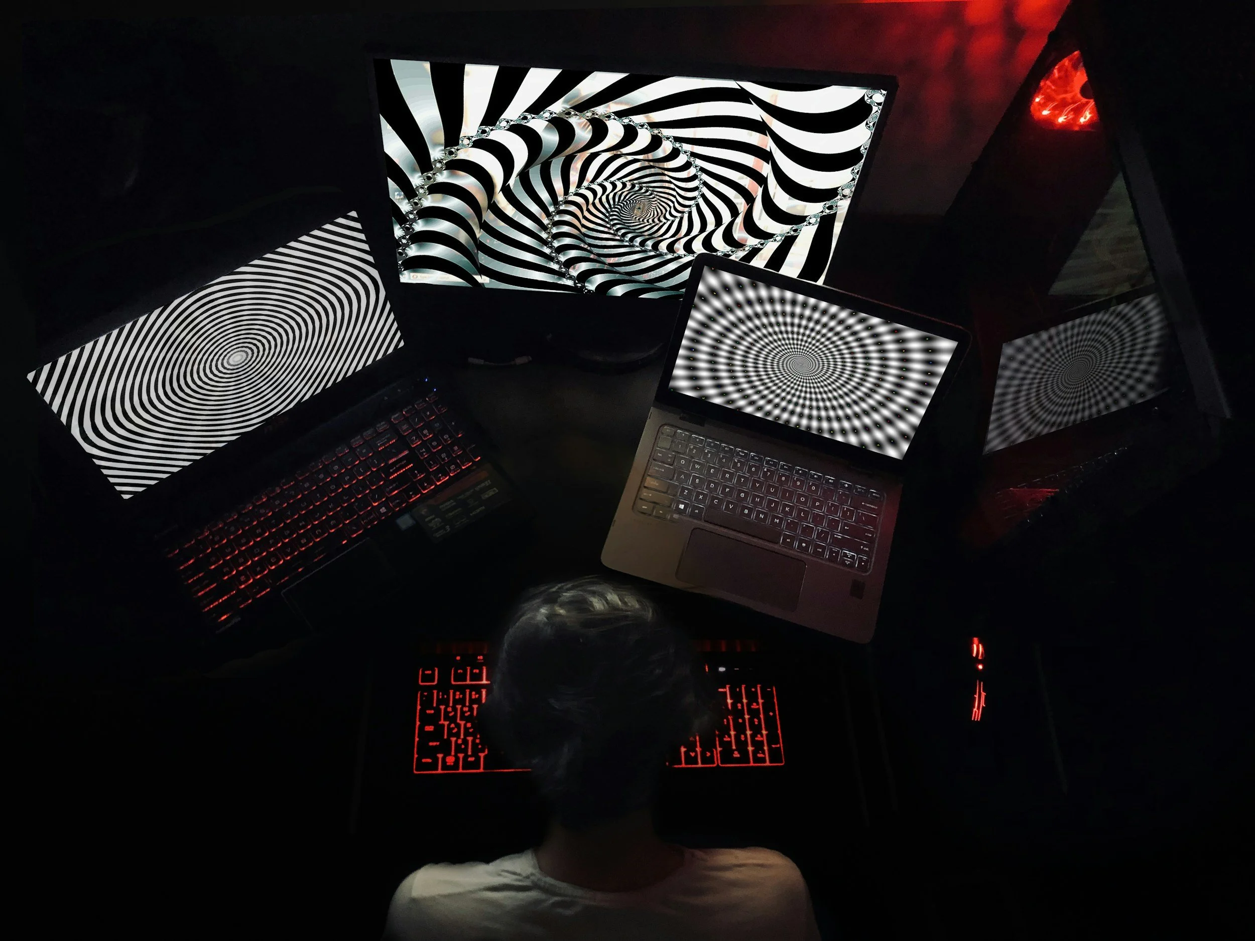 Person sitting at a desk with multiple computers displaying swirling black and white hypnotic patterns, creating a visually intense scene.