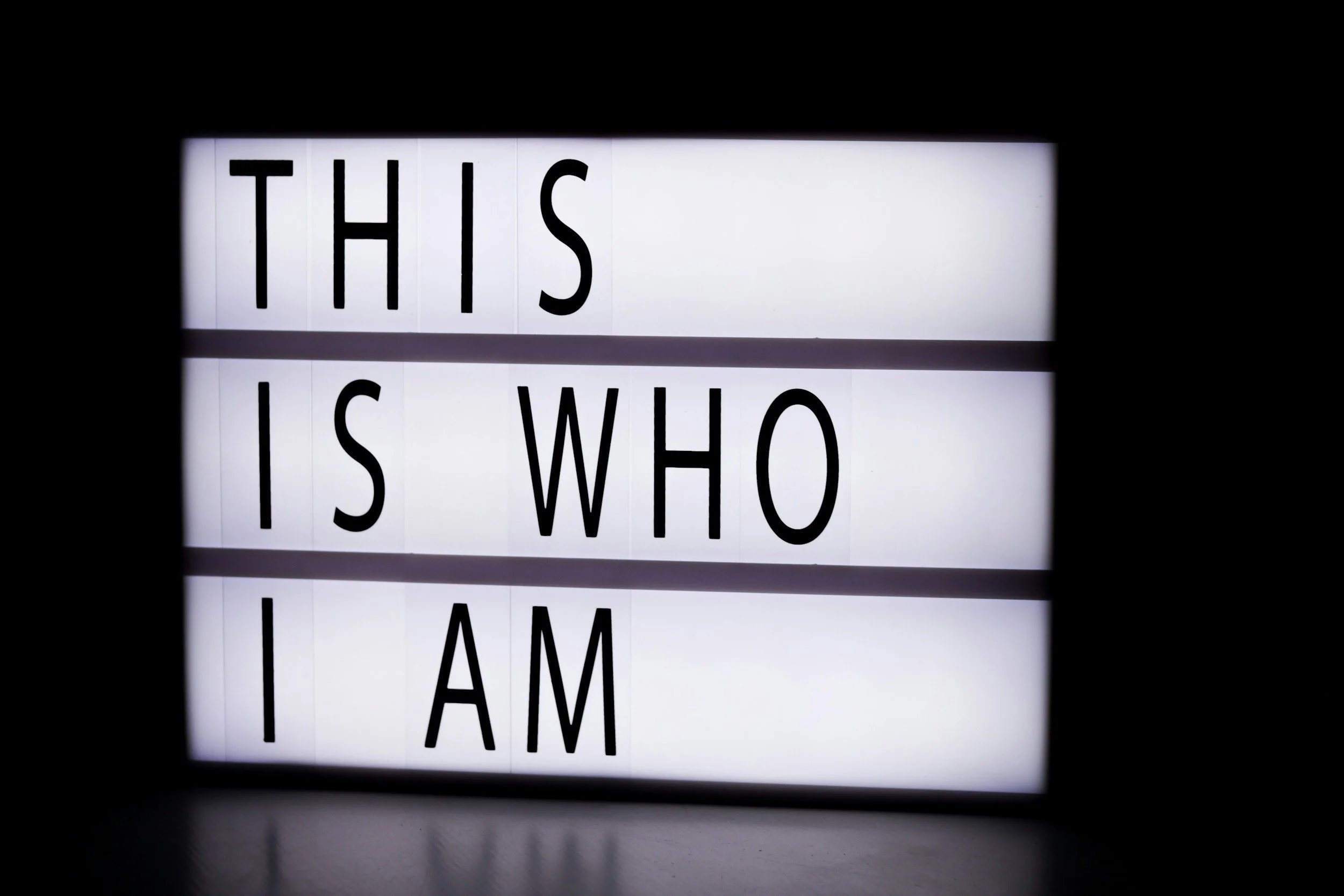 A lightbox sign with the words 'This is who I am' displayed in black letters against a white background, with black borders on the sides.