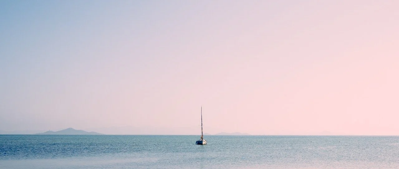 Un velero en el mar con cielo despejado y pequeñas islas al fondo.