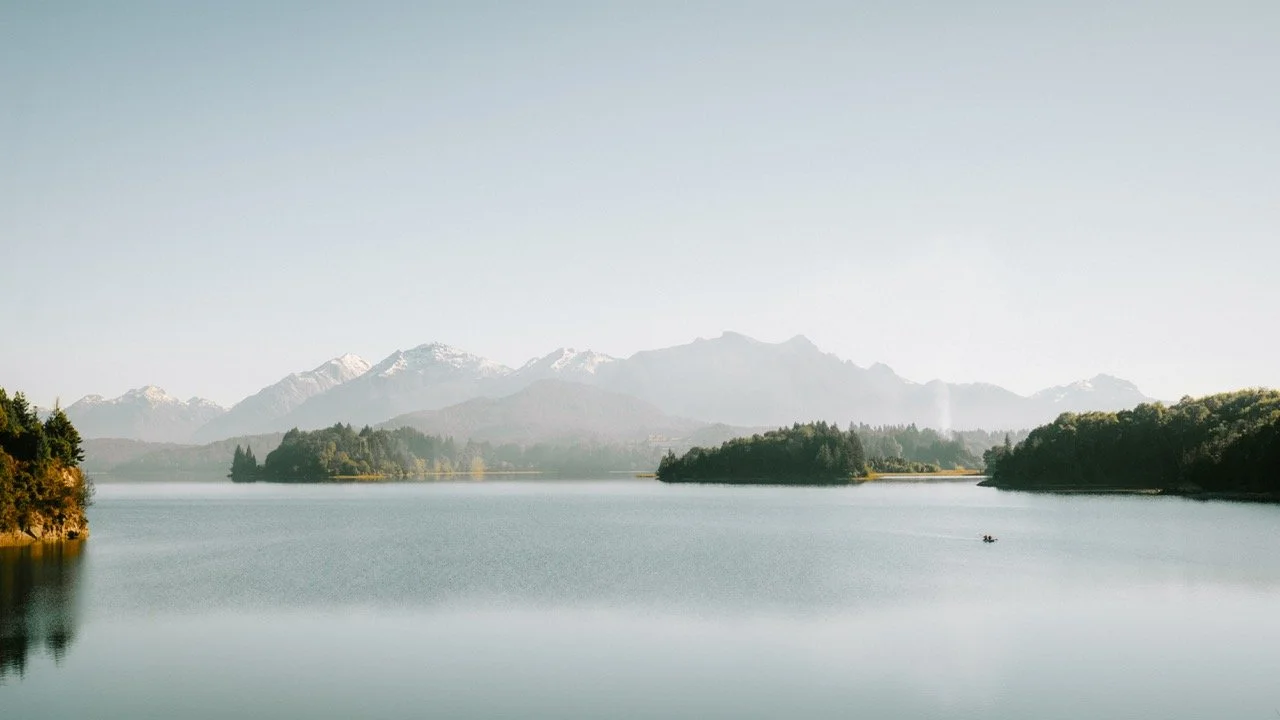 Vista de un lago con montañas nevadas al fondo y islas cubiertas de árboles, en un día despejado.