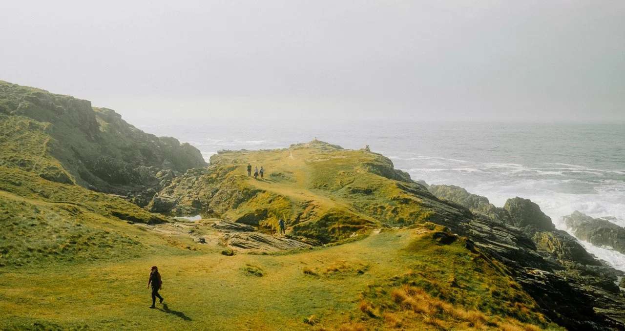 Paisaje costero con acantilados y personas caminando por un sendero en la hierba.