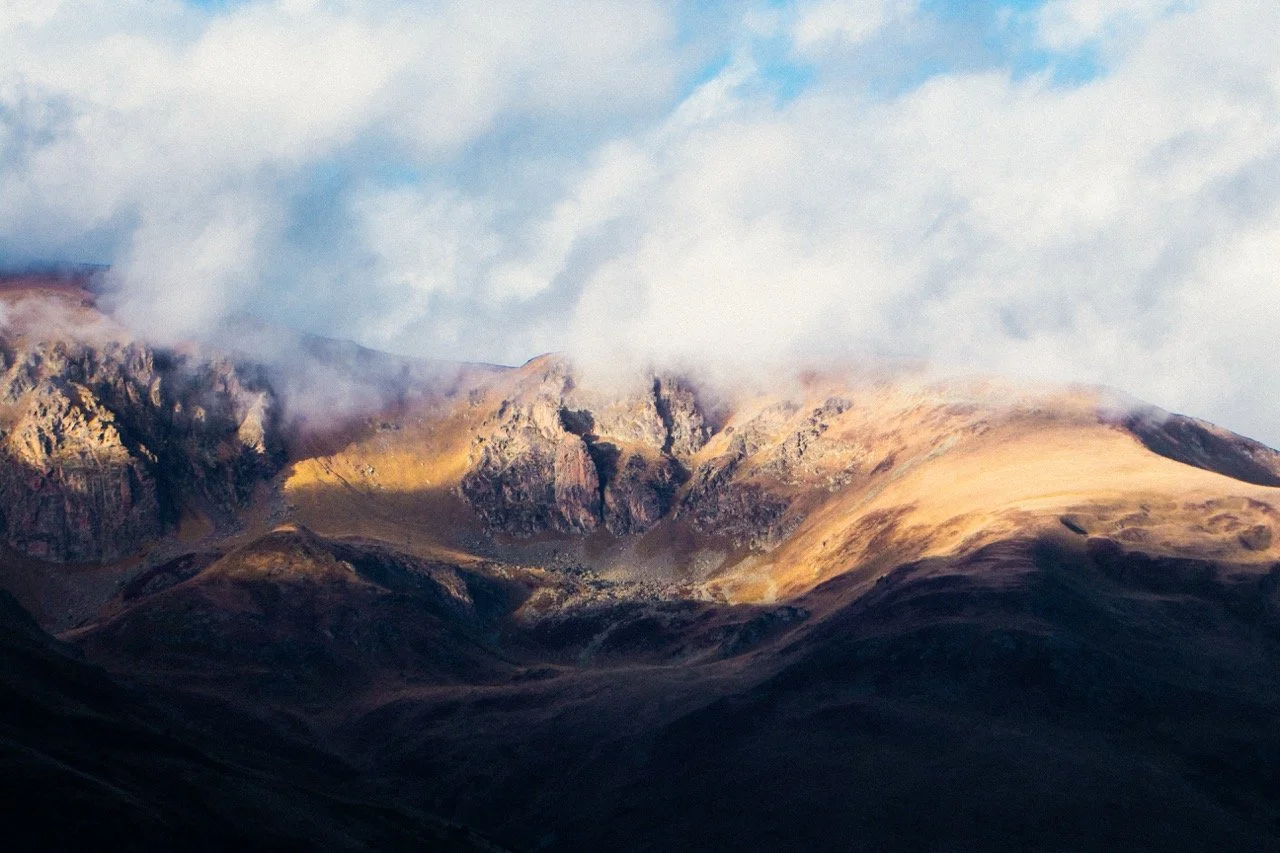 Montañas con picos rocosos y niebla en la cima, cielo parcialmente nublado en un paisaje natural