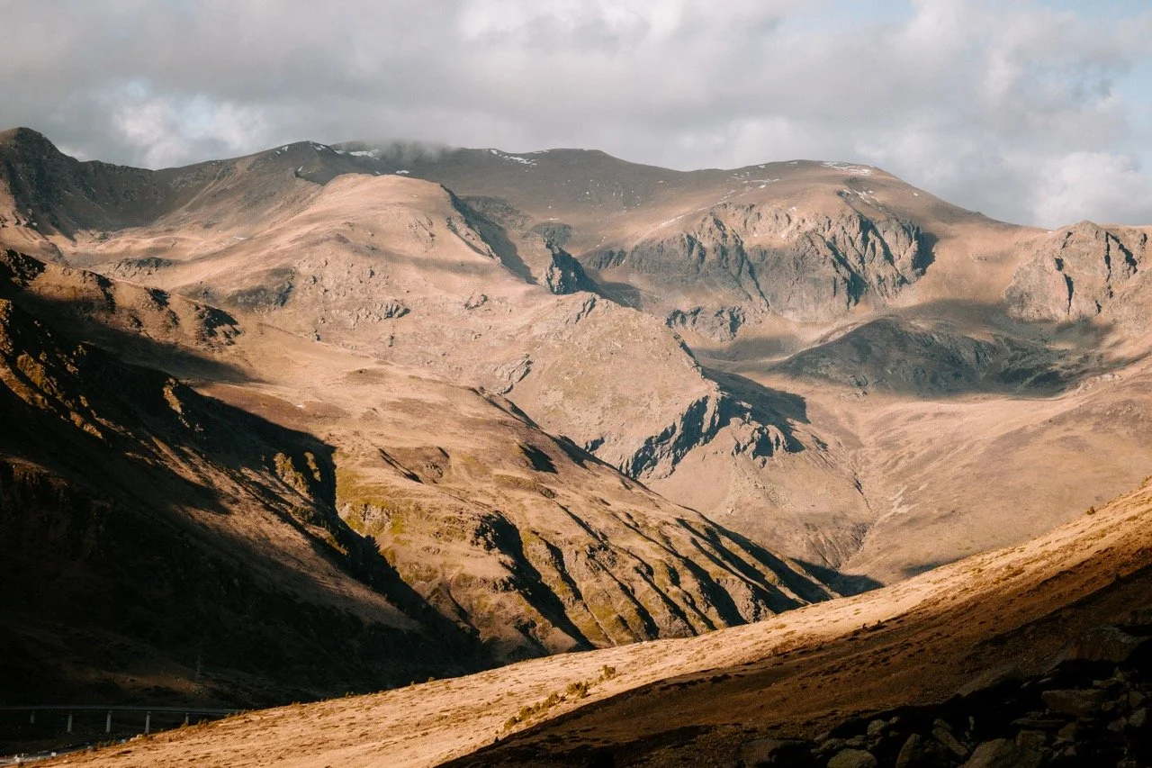 Montañas áridas con pendientes escarpadas y poco vegetación, bajo un cielo parcialmente nublado.