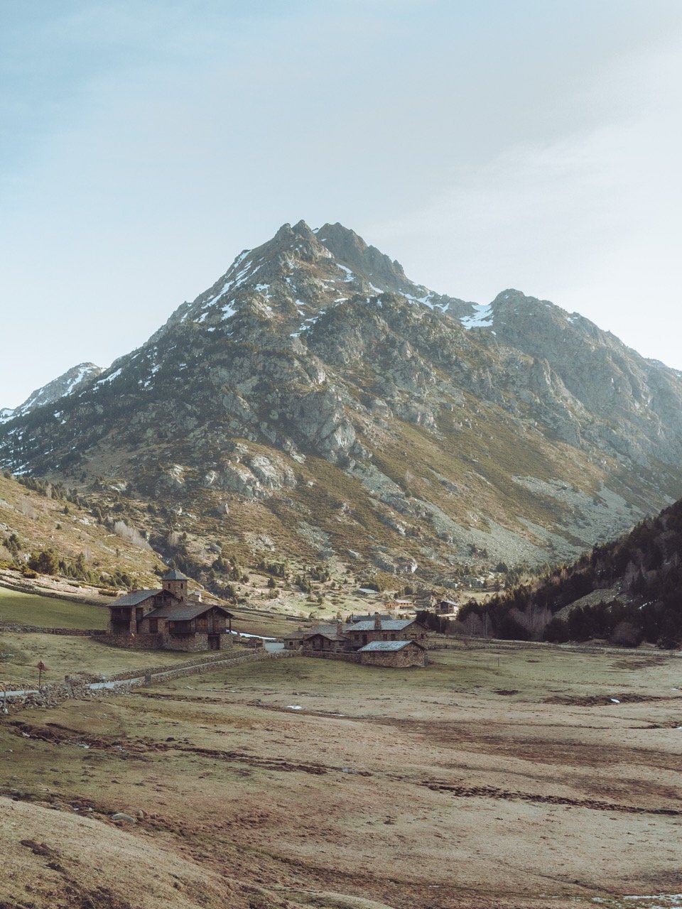 Montaña grande con nieve y un cielo despejado, y en el terreno cercano, varias casas de madera en un valle agrícola