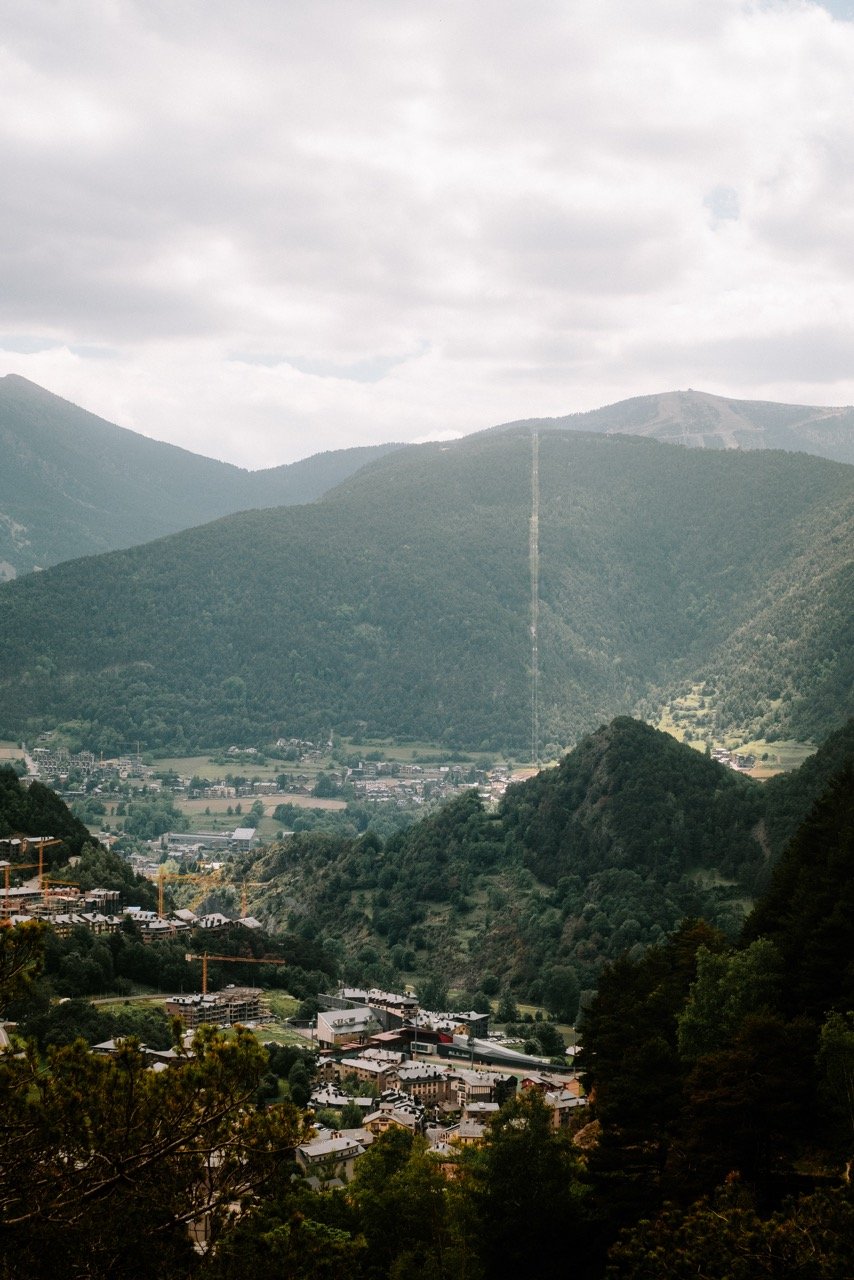 Vista de un valle rodeado de montañas con un pequeño pueblo en el centro y nubes en el cielo.