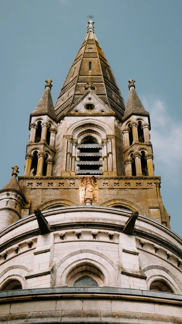 Vista desde abajo de una iglesia gótica con una torre alta y detalles ornamentales en piedra.