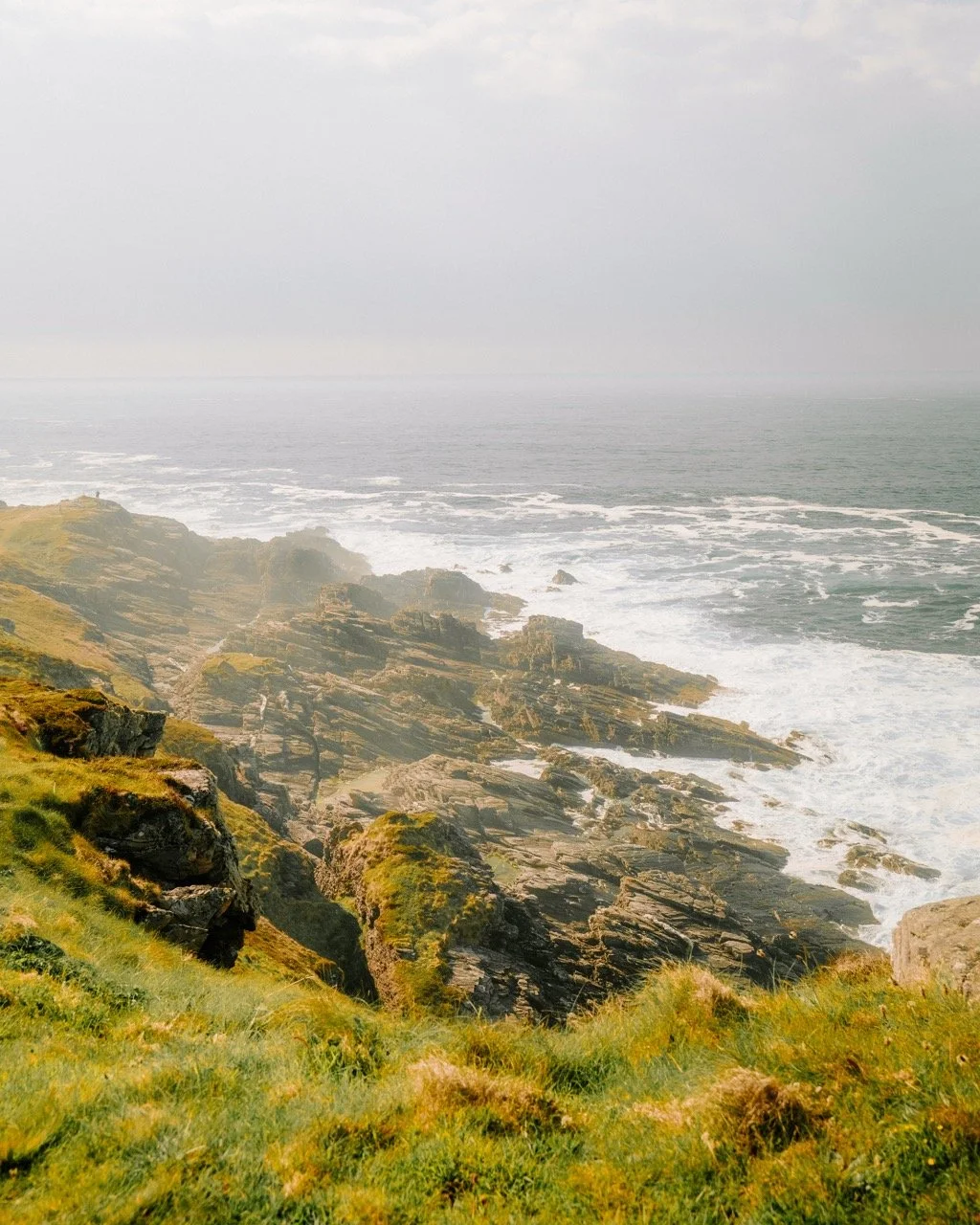 Costas rocosas y verdes con olas del mar en un día nublado.