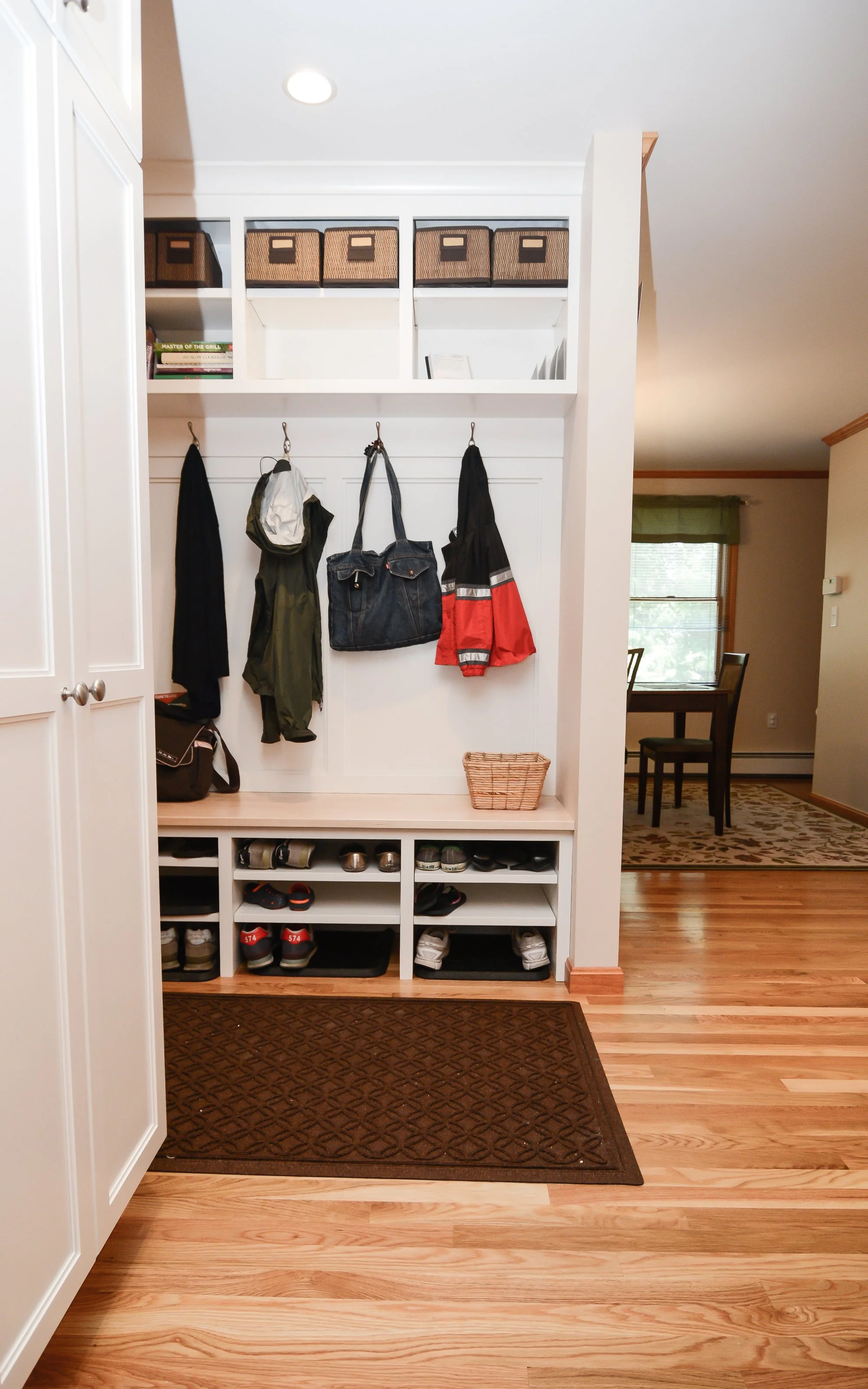 Entryway with hooks holding jackets and bags, shelving with shoes, baskets, and storage bins