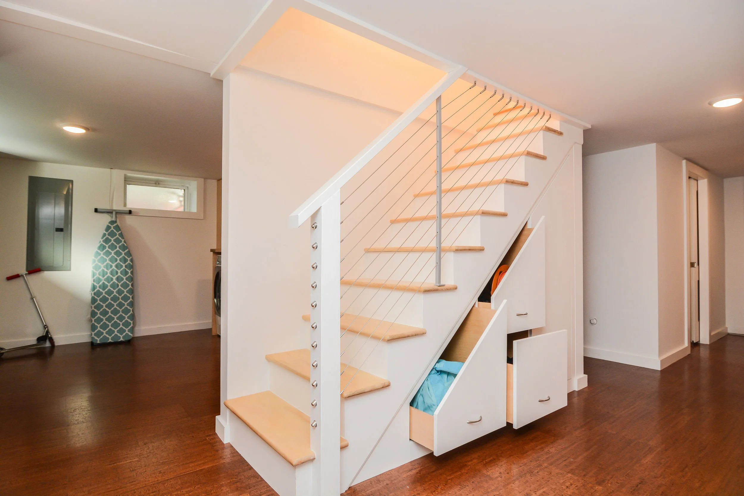 Wood staircase with white railings and built-in storage drawers underneath, inside a room with wood flooring.