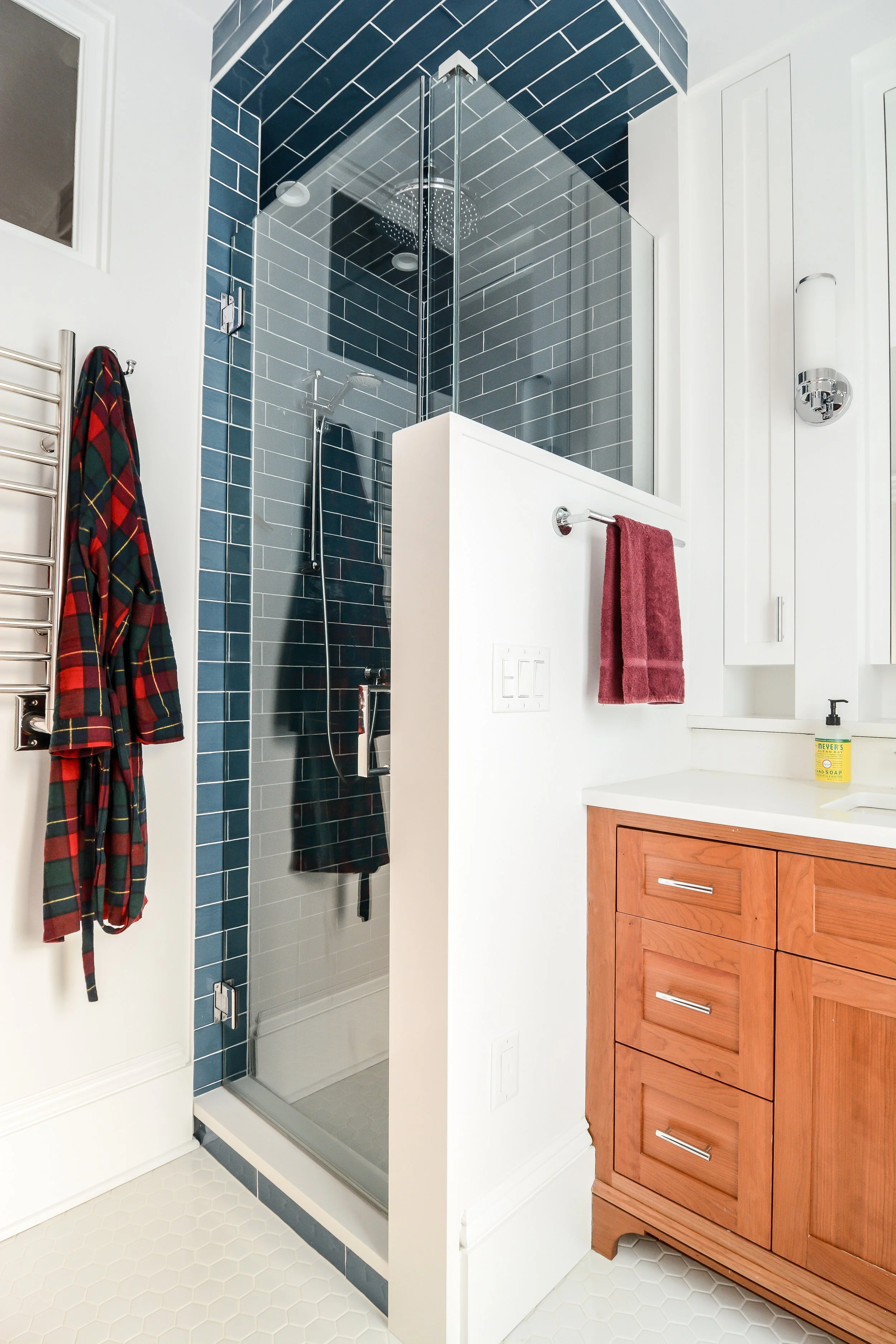 Bathroom with a glass shower, white walls, wooden vanity, and colorful towels.