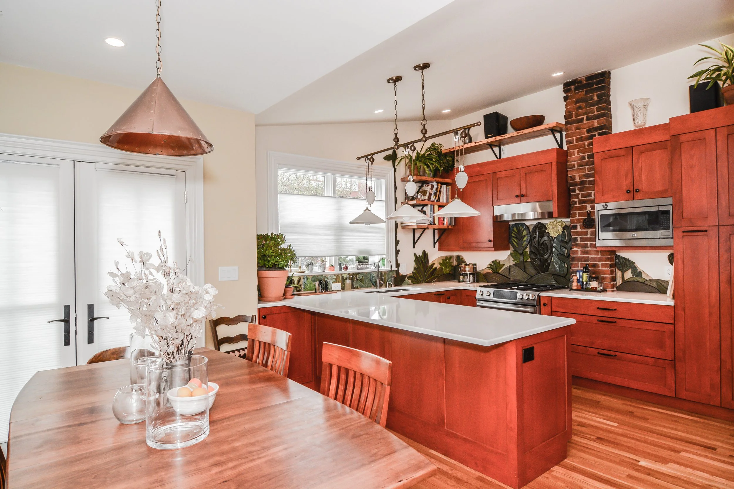 Kitchen with red wood cabinets, white countertops, brick chimney, black stove, and wooden dining table with chairs