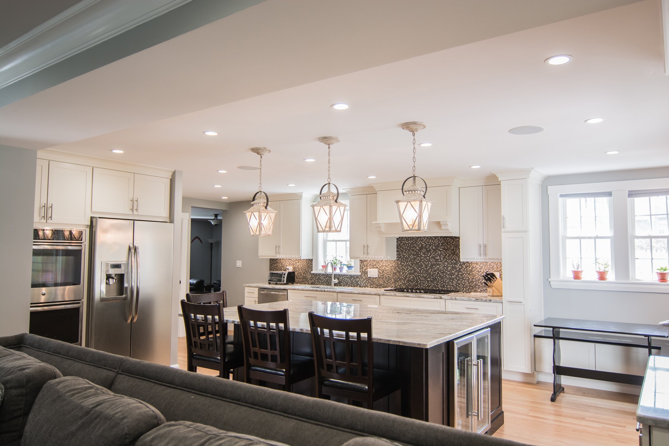 Modern kitchen with white cabinets, granite island, stainless steel appliances, black backsplash, and pendant lights