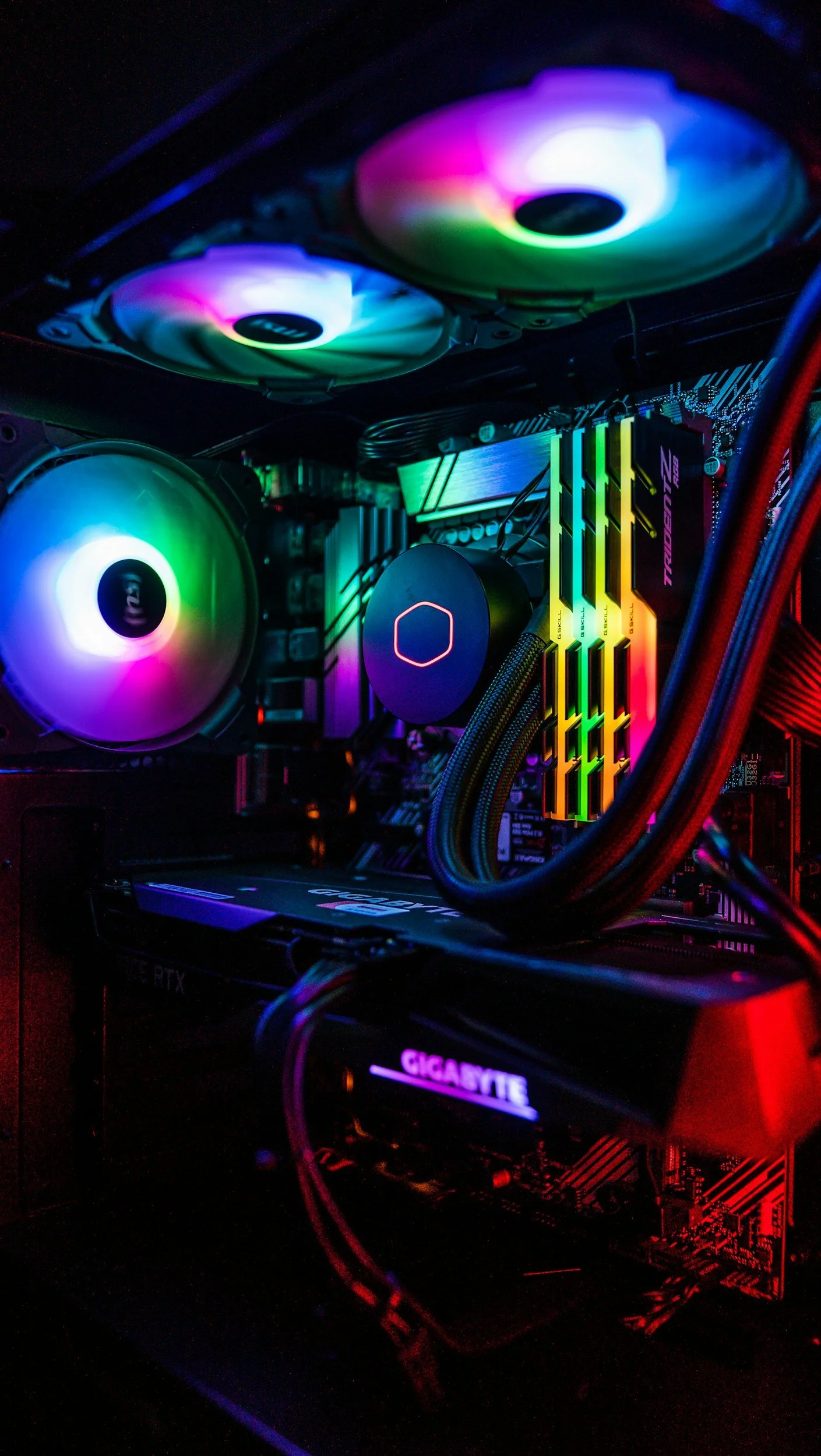 Inside a gaming computer with colorful RGB lighting, including cooling fans, RAM sticks, a CPU cooler, and a graphics card.