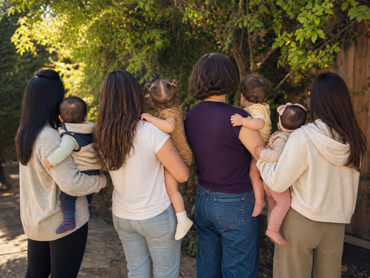 Group of women holding young children outdoors near a tree