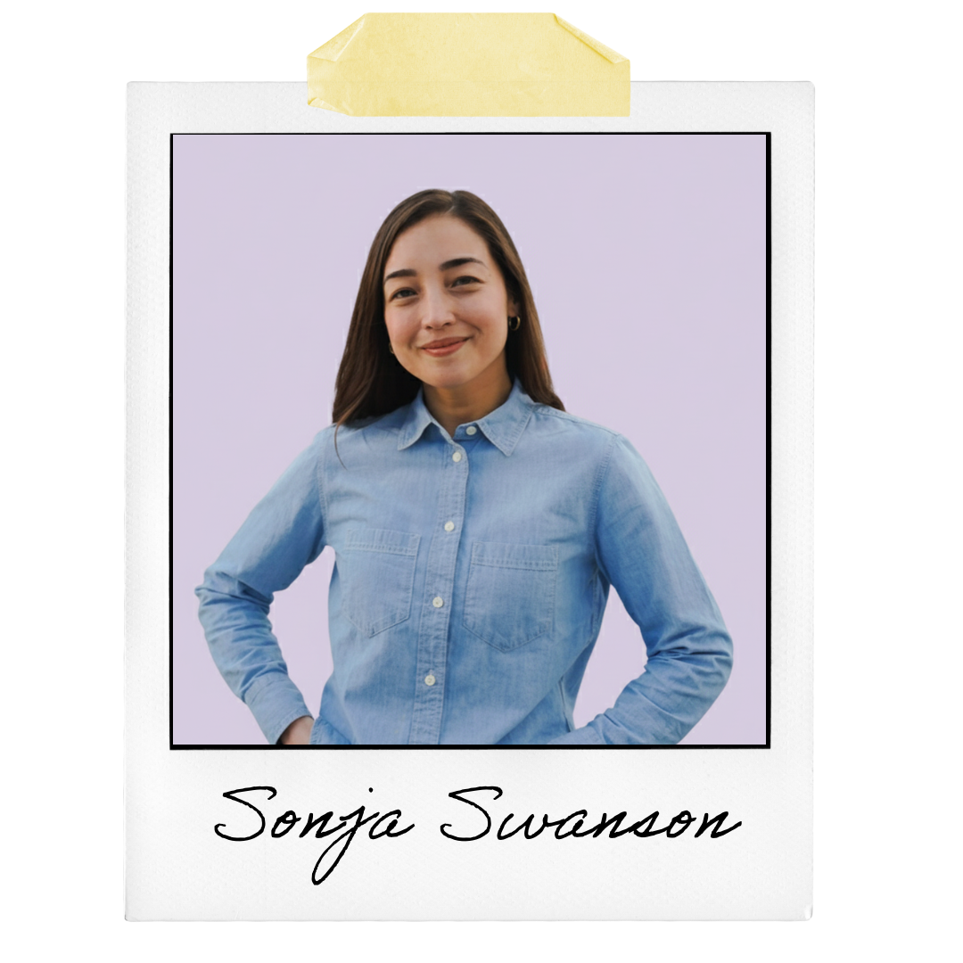 Photograph of a woman with long brown hair, wearing a light blue denim shirt, smiling with one hand on her hip against a light purple background