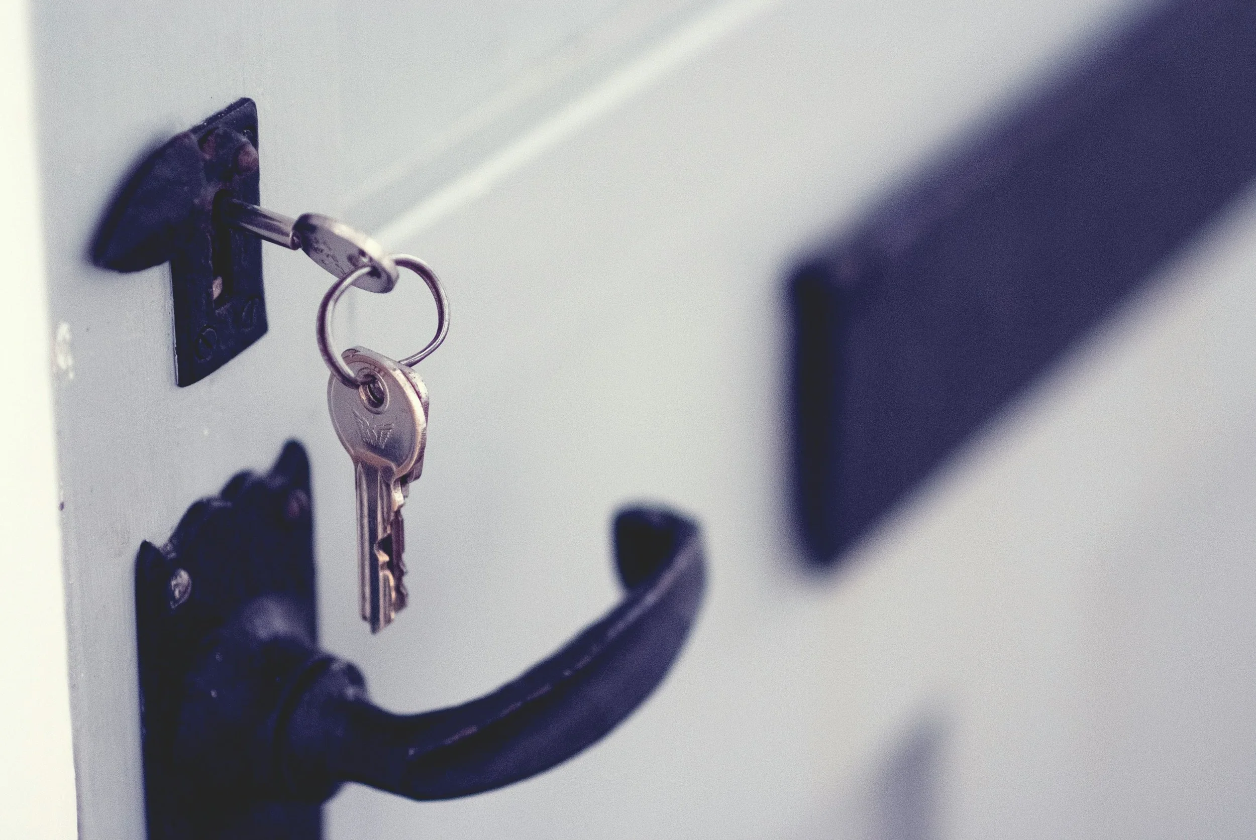 A close-up of a metal key inserted into a locker lock, with a keyring holding two keys hanging from the lock.