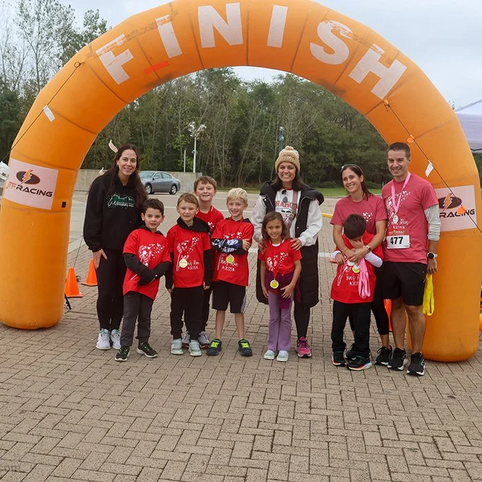 Group of children and adults standing under a large orange inflatable finish line arch at a race event.