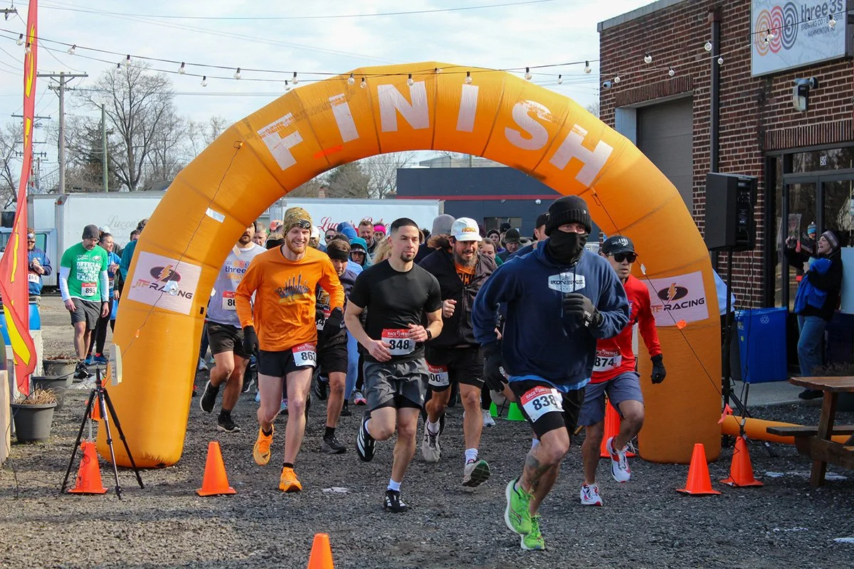 A group of runners crossing the finish line under an orange arch labeled 'FINISH' during a race event.