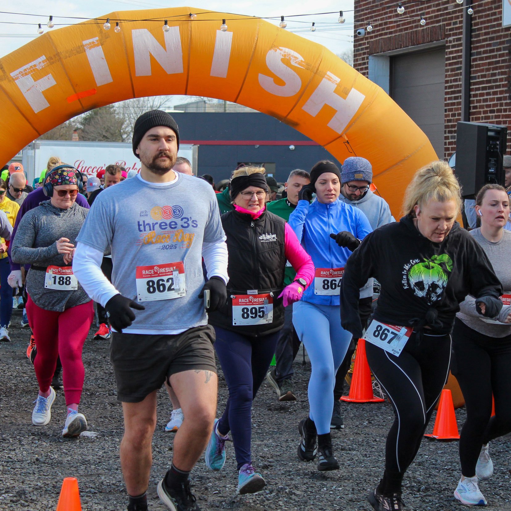 Group of people participating in a race or marathon, running under the finish line arch that says 'FINISH', some wearing race bibs, dressed in athletic clothing and outerwear.