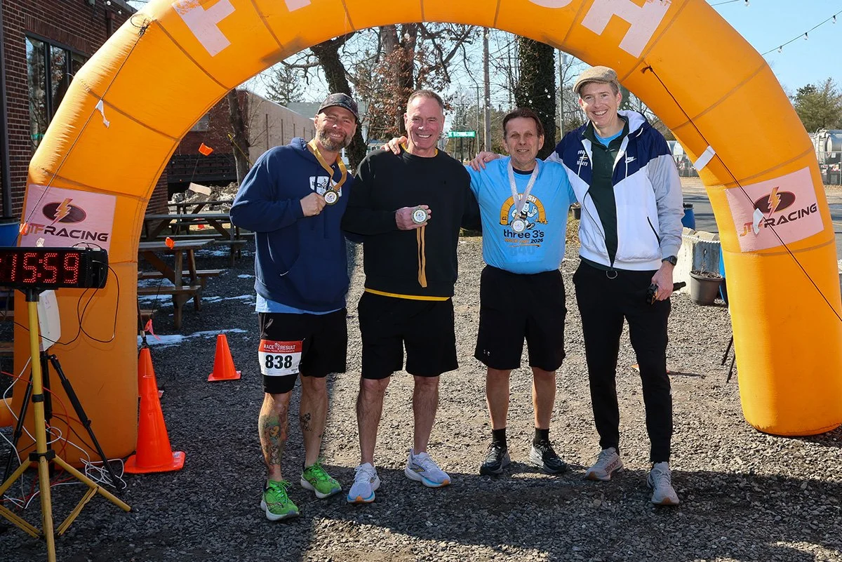 A group of runners posing for a photo under the JTF Racing inflatable finish archway.