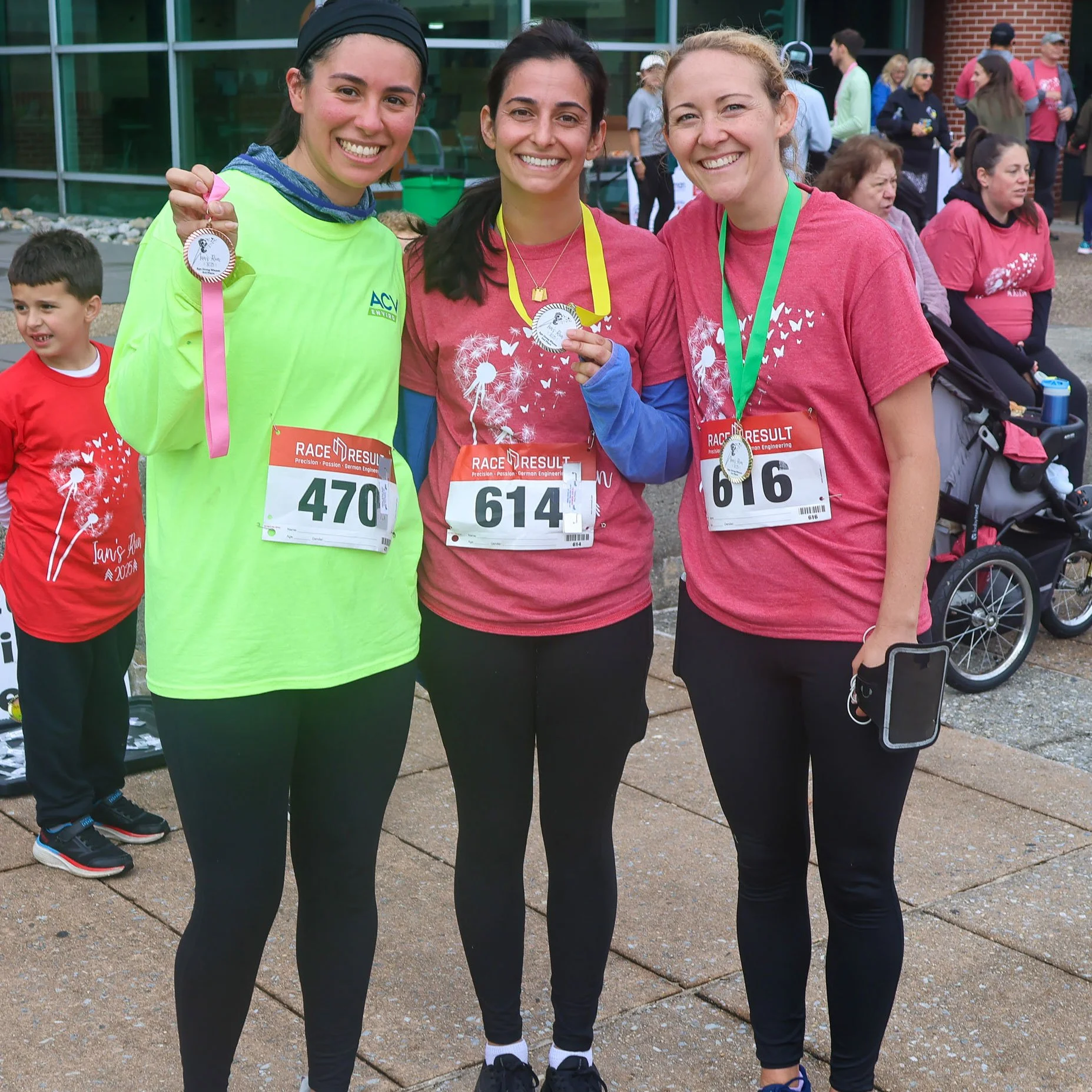 Three women with race medals and bibs at a running event, smiling and posing together outside.