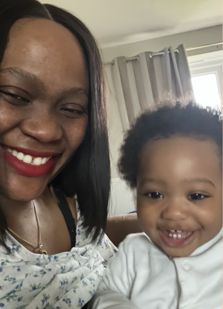 A smiling woman with dark hair and red lipstick taking a selfie with a smiling young girl with curly hair.