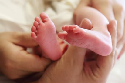 Close-up of a person's hand gently holding two tiny baby feet