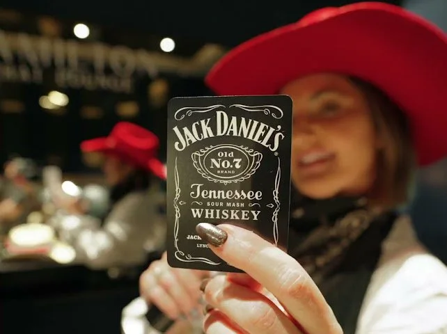 A person wearing a large white cowboy hat with feathers, leaning over a table filled with sewing and craft supplies, including colorful threads, buttons, and fabric.