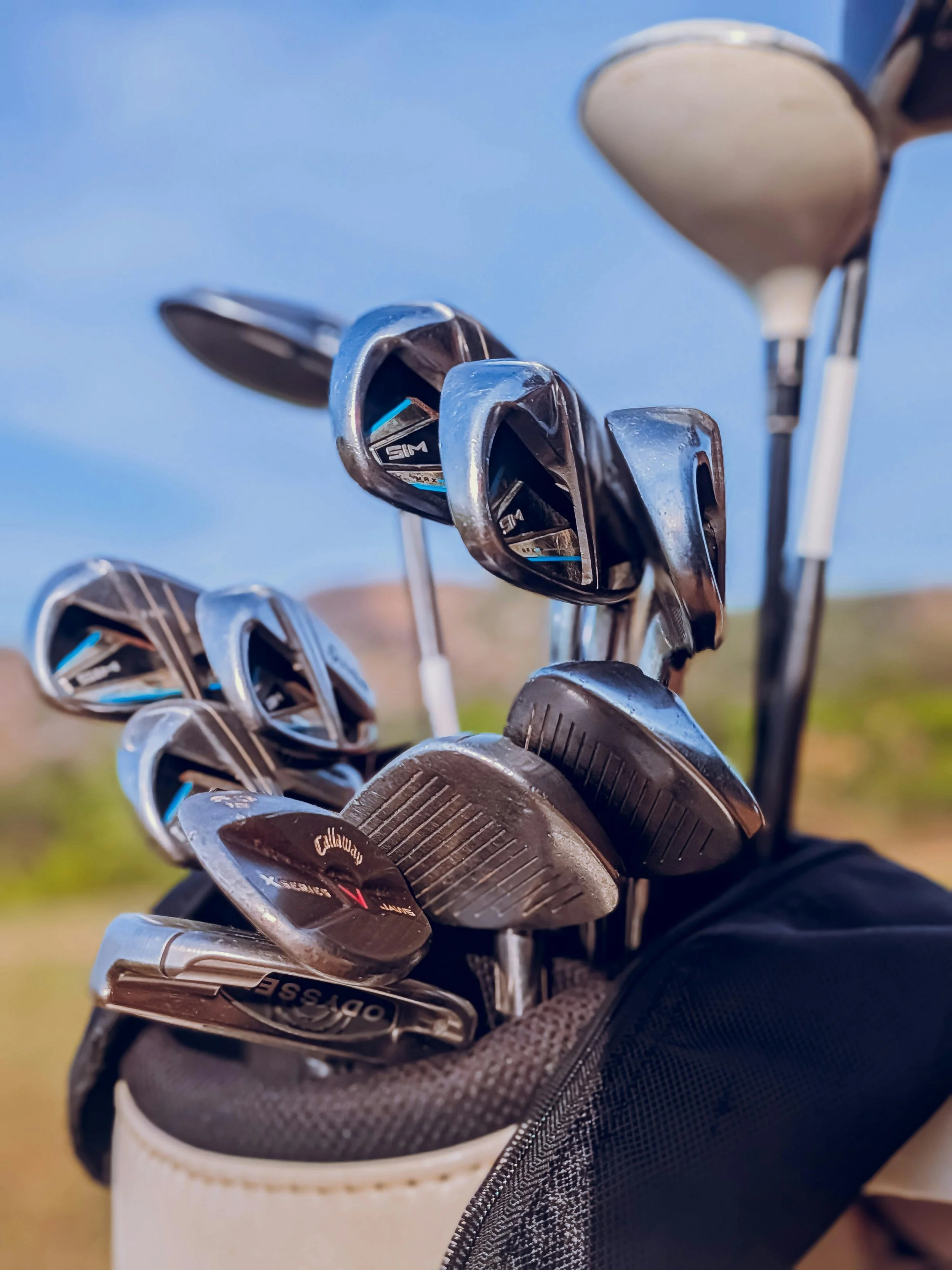 Set of golf clubs in a golf bag, including woods, irons, and a putter, outdoors with a clear sky.