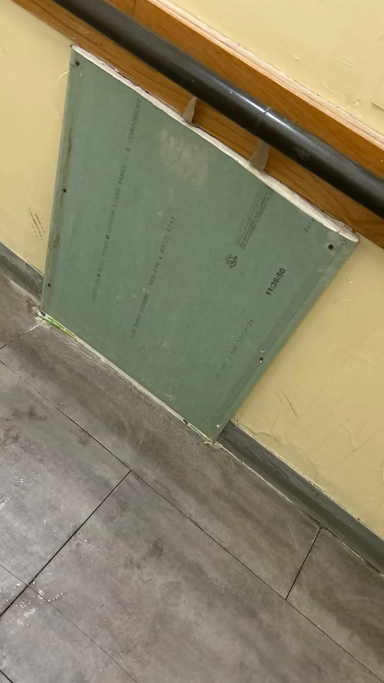 A metal panel leaning against a yellow wall, near a black handrail and gray tiled floor.