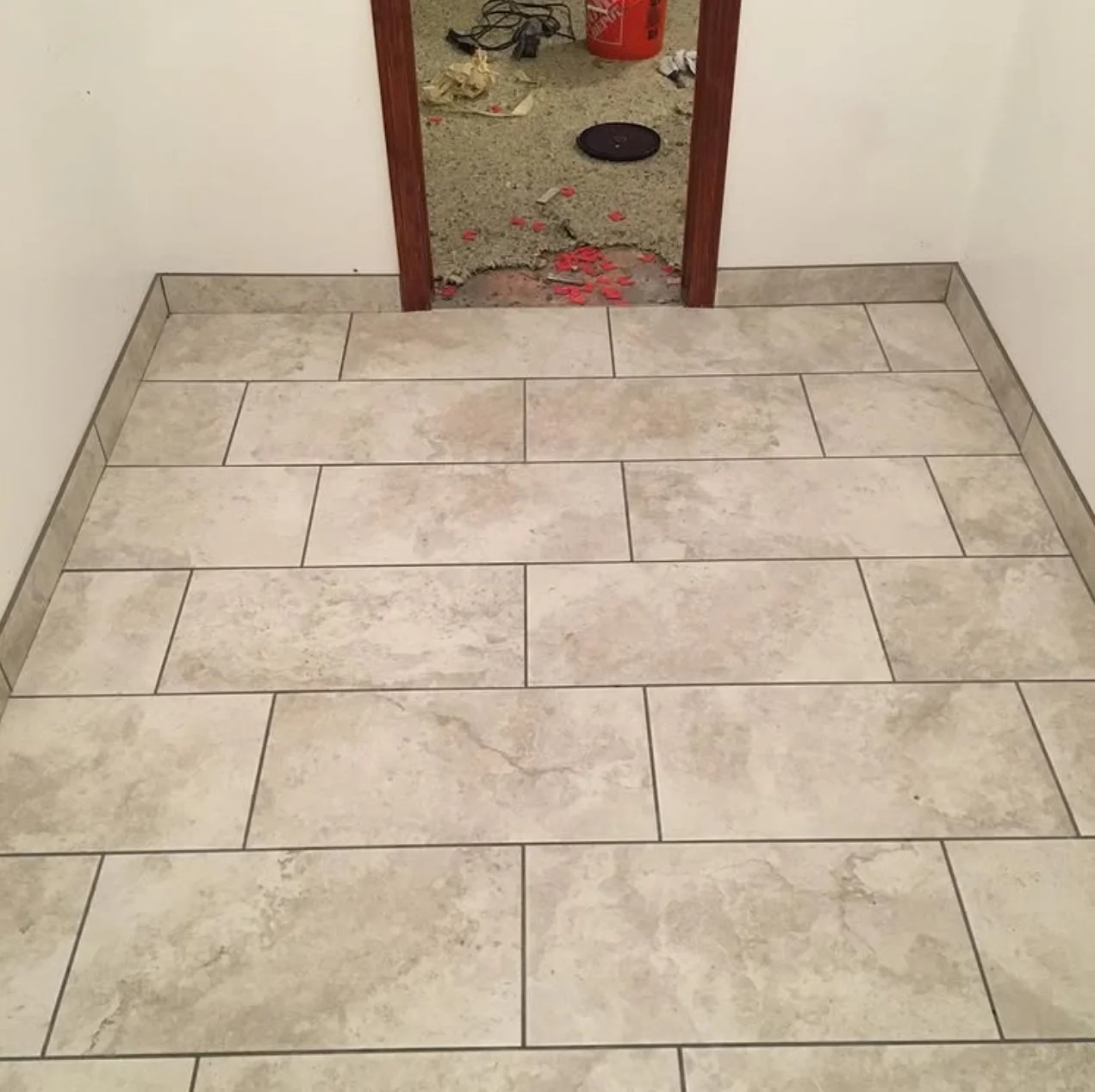 Clean tiled floor near a doorway, with a construction or renovation area visible through the door opening, showing debris and tools.