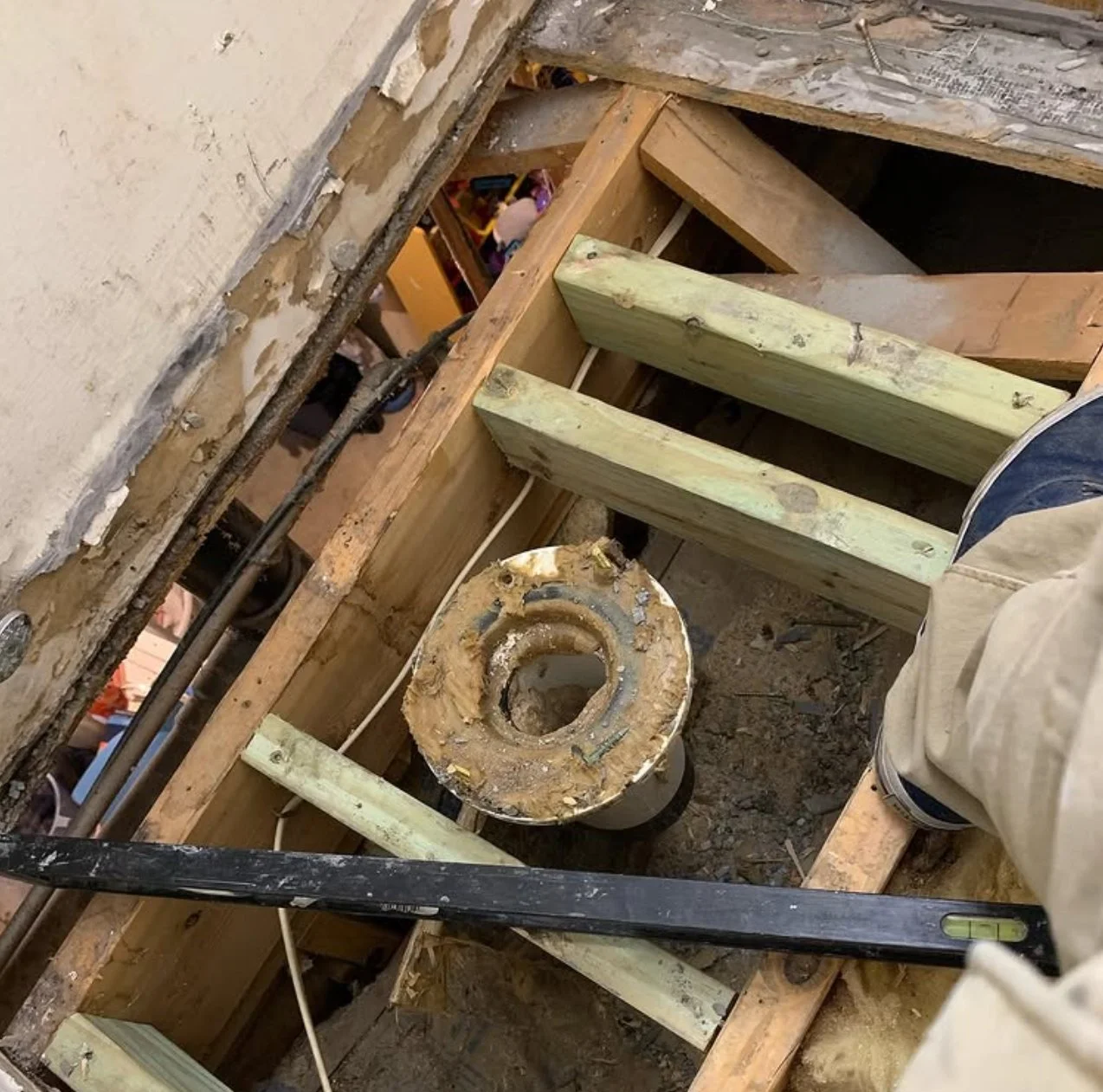 View of a bathroom area with a damaged toilet, exposed wooden framing, and plumbing pipes during renovation.