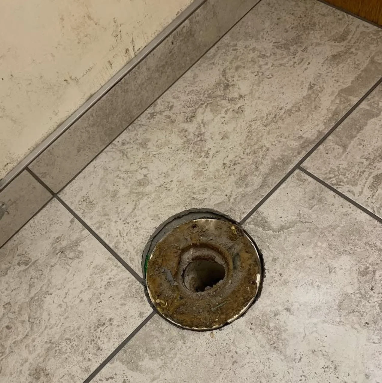 A bathroom floor with a removed or broken toilet flange showing rusted metal and debris around the opening.