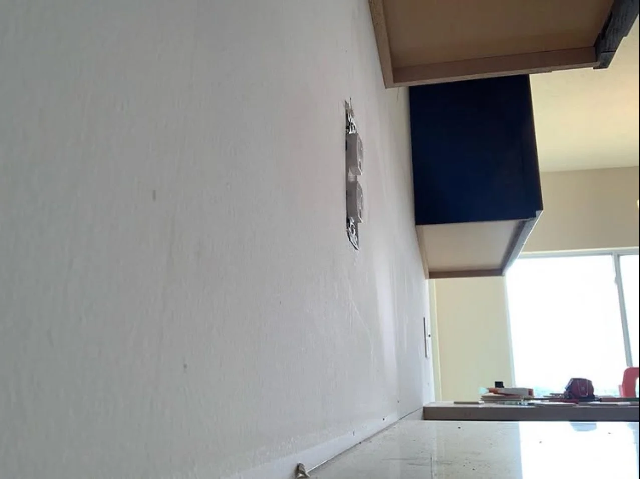 Empty room with beige carpet, brown and dark blue furniture, window allowing natural light, and some electrical outlets or switches on the wall.