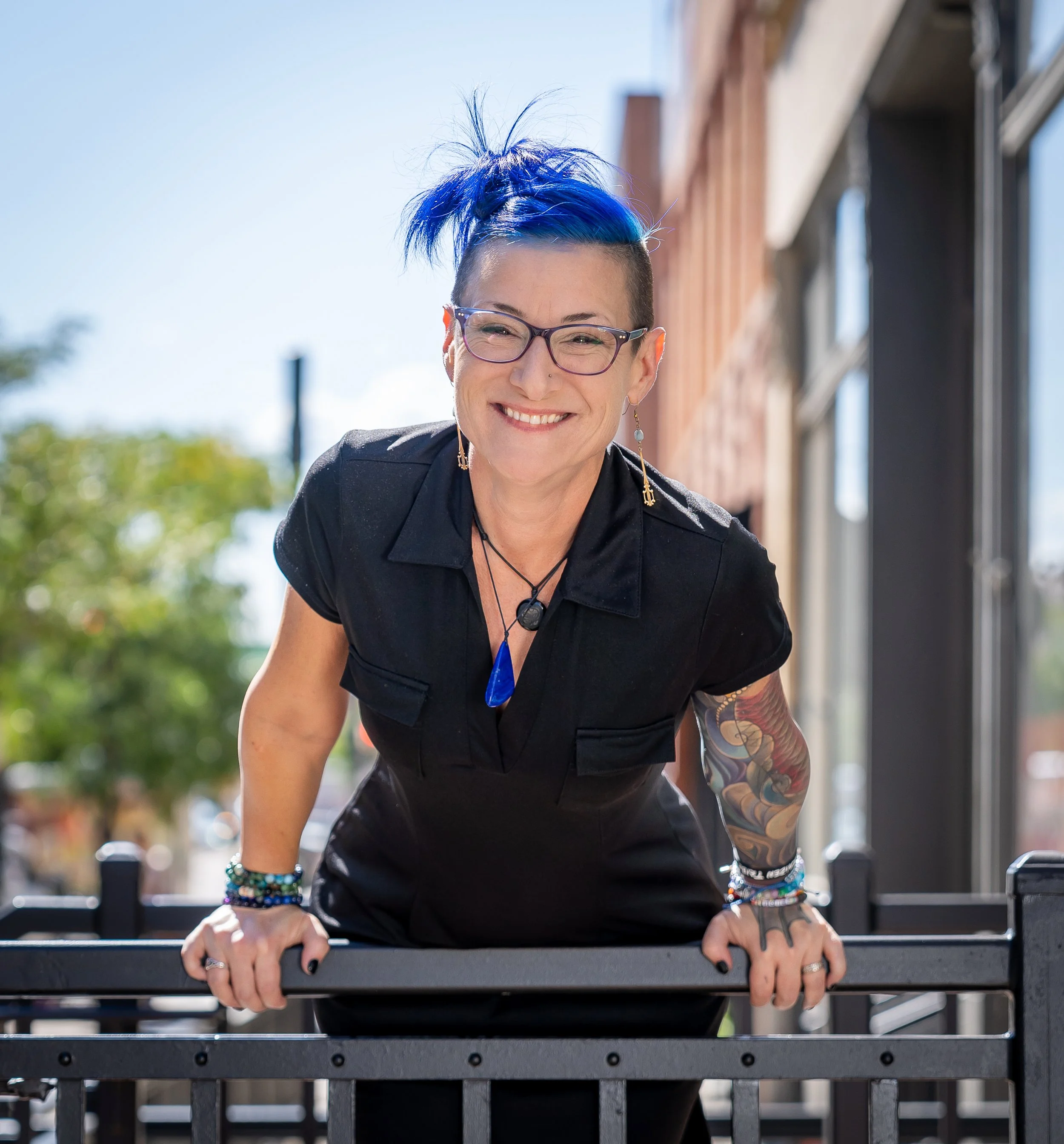 Woman with blue hair and glasses smiling while doing push-ups outside on a sunny day.