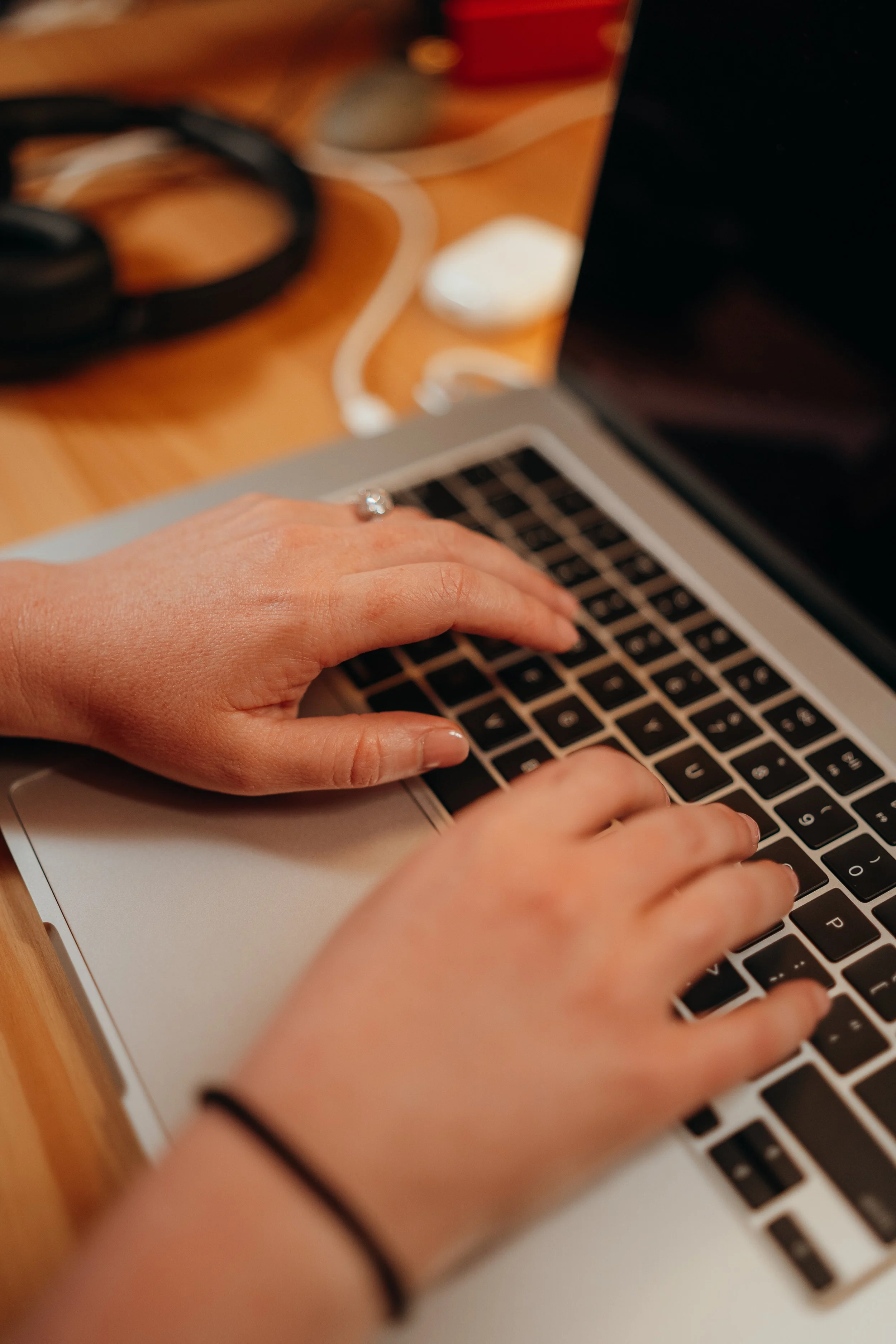 Hands typing on a laptop beside headphones on a wooden table