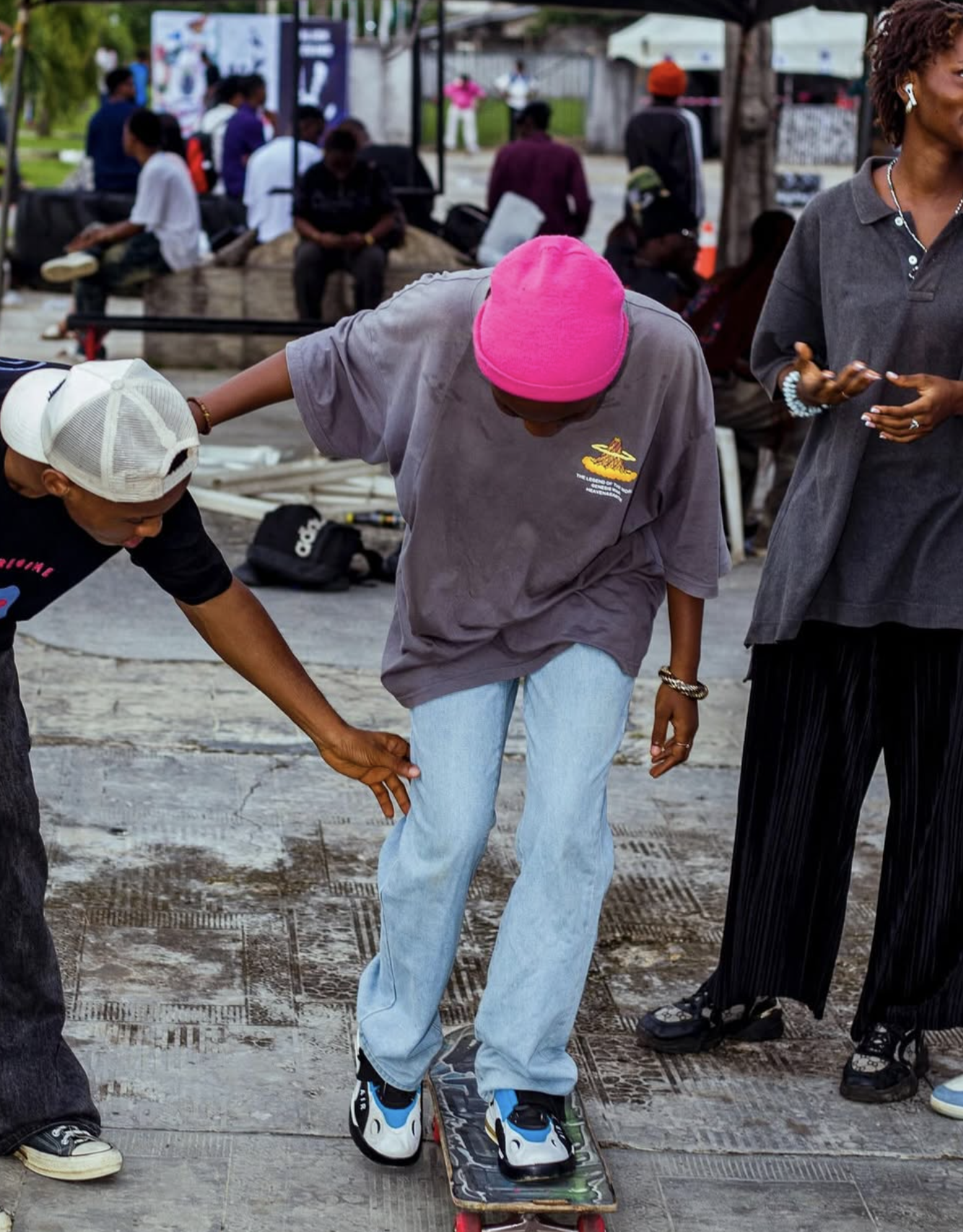 A woman is skateboarding outdoors with assistance from two men, on a city street on a cloudy day.
