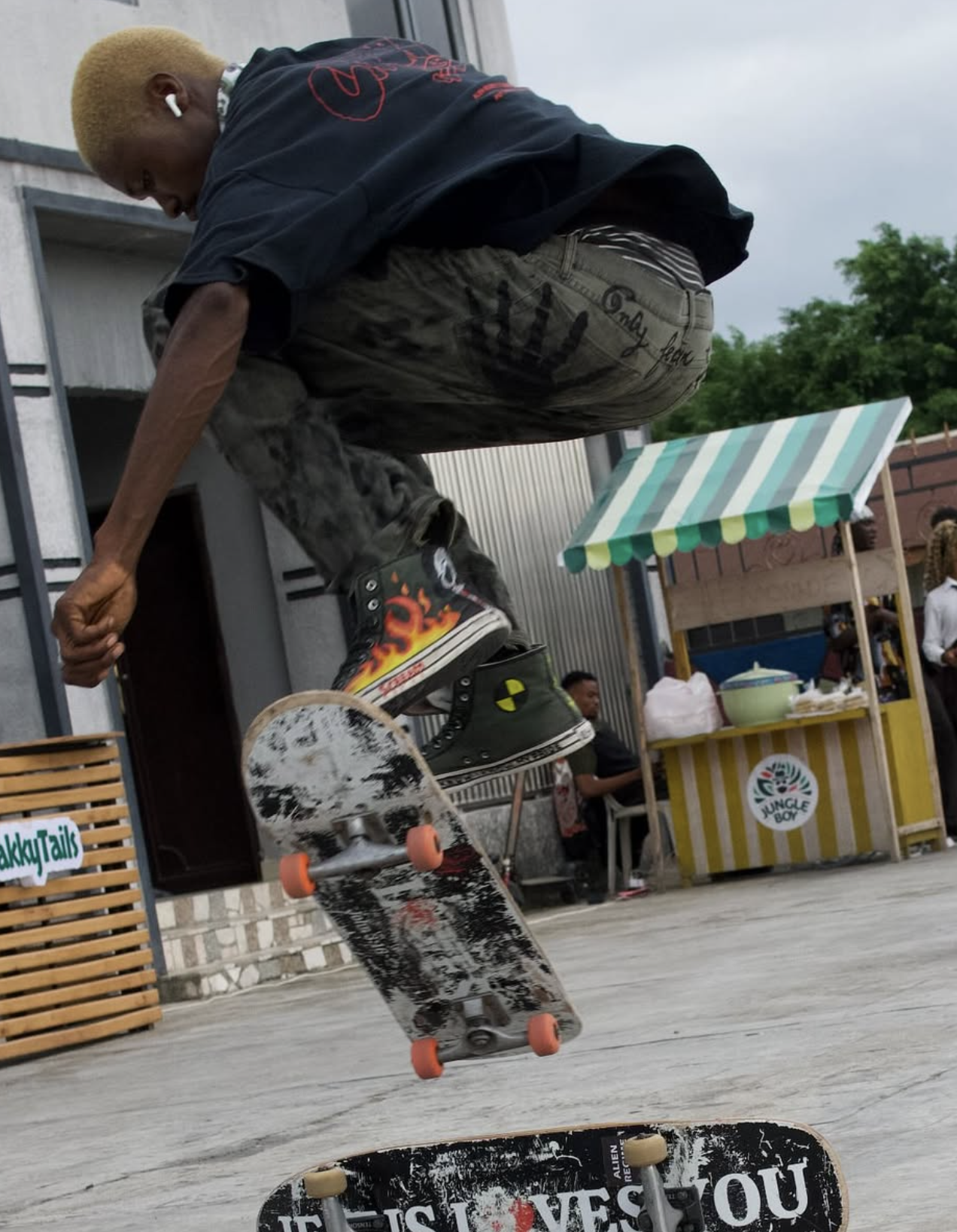 Skateboarder mid-air performing a trick outdoors near a street food stand and people.