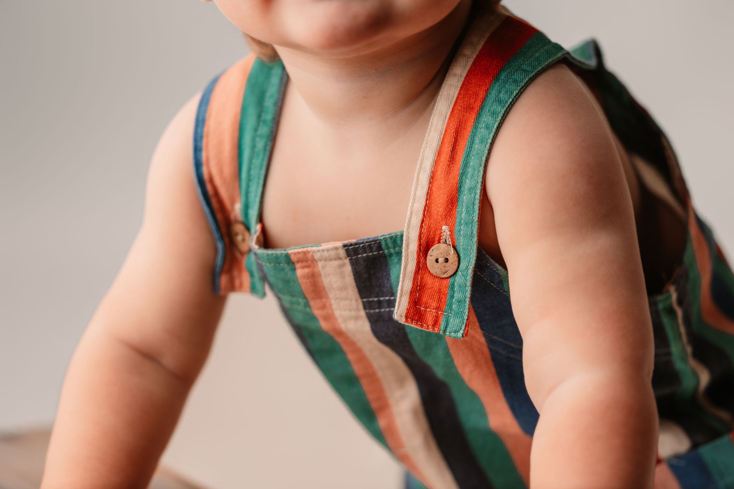 Small button details on striped colorful overalls with a neutral backdrop. Children's store in dahlonega