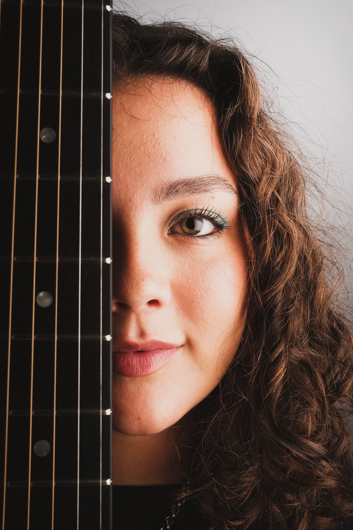 Närbild av en ung kvinna med lockigt brunt hår som tittar fram bakom en gitarr.