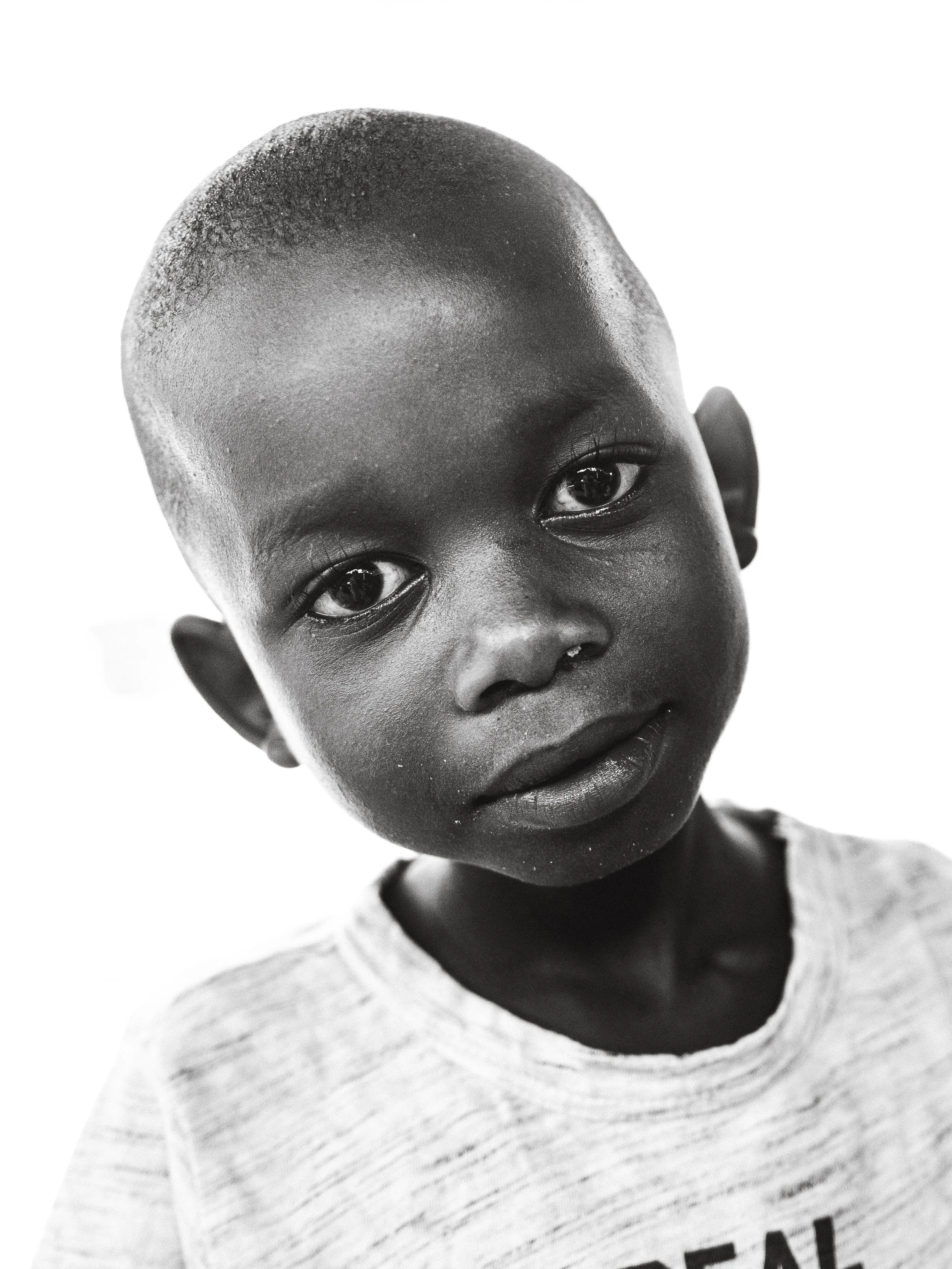 Svartvit bild av en ung pojke med kort hår och mörk hud, som tittar mot kameran.